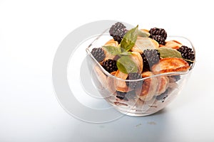 Minipancakes with blackberries and mint leaves in a glass cup on a white background