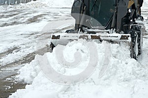 Minitractor bucket clears snow from the neighborhood after a snowstorm. Fragment.