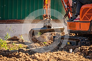 A minitractor rakes the earth with a bucket. Land works.