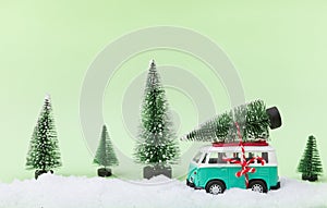 Minivan car carrying a Christmas tree in a snow covered miniature evergreen forest
