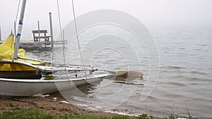 A Minnesota lake beach on a foggy morning with a boat dock and beached sailboat.