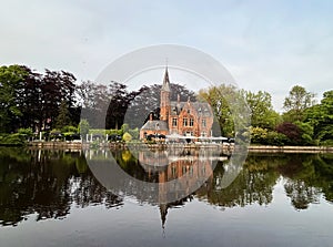 Minnewater ancient medieval red brick castle at the Lake of Love in Bruges in public park zone, Belgium