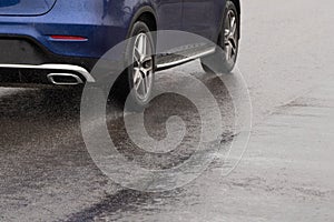 minor rain water splash flow from wheels of blue car moving fast in day light city with selective focus