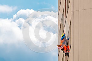 Industrial climber washes windows on facade of a building. Side view with sky and clouds