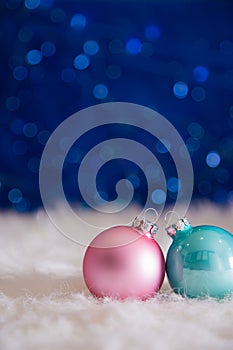 Mint blue and pink Christmas balls on white fur with garland lights on blue bokeh background