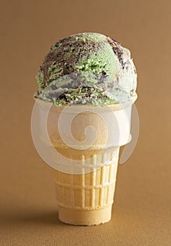 Mint Chocolate Chip Ice Cream Cone on a Chocolate Brown Background
