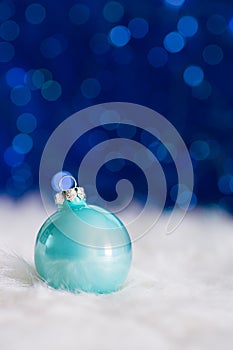 Mint Christmas ball on white fur with garland lights on blue bokeh background