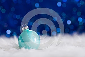 Mint Christmas ball on white fur with garland lights on blue bokeh background