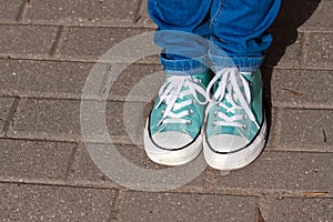 Mint youth sneakers, shod on legs in blue jeans, on paving tiles