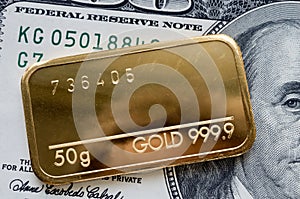 Minted gold bar weighing 50 grams against the background of dollar bill