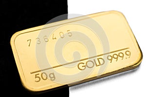 Minted gold bar weighing 50 grams on a black and white background.