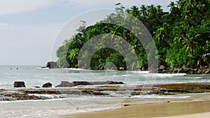 Mirissa beach lagoon in Sri Lanka with waves crashing on rocky shore. Palm trees sway, tropical scenery entices for