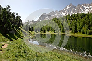 Miroir lake located above Ceillac village after one hour hike, with reflections of mountain range covered with snow and pine trees