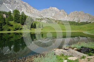 Miroir lake located above Ceillac village after one hour hike, with reflections of mountain range and pine tree forests