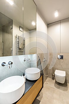 Mirror above white washbasins in beige bathroom interior with li