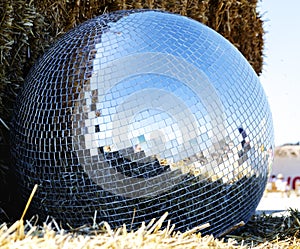 Mirror ball from a disco lies on a straw outdoors