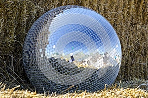 Mirror ball from a disco lies on a straw outdoors
