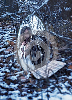 In a mirror in the middle of a winter forest, an angel with black wings is reflected.