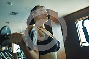 Mirror portrait of young pretty and fit Asian Chinese woman working hard at hotel gym or fitness center lifting dumbbell doing