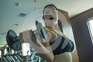 Mirror portrait of young pretty and fit Asian Japanese woman working hard at hotel gym or fitness center lifting dumbbell doing