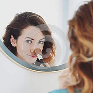 Mirror portrait of a young woman powdering her nose