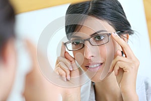 Mirror portrait of young woman trying on eyeglasses