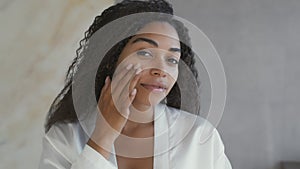 Mirror pov of young attractive african american lady applying moisturizing cream on face, taking care about appearance