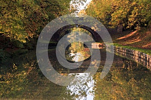 Mirror Reflection of Arched Bridge and autumn Trees in the Grand Union Canal