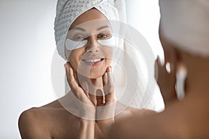 Mirror reflection attractive 30s lady with eye area care patches.