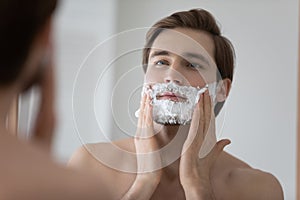 Mirror reflection close up young man applying shaving foam