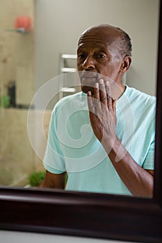 Mirror with reflection of concerned senior man touching his cheek