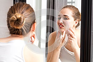 Mirror reflection of girl with acne squeezing her pimples