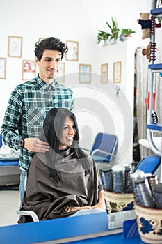 Mirror reflection of hairstylist hairdresser with comb combing hair of female client. Woman in hairdressing beauty salon