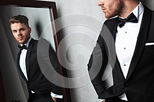 Mirror reflection of relaxed young man wearing a black tuxedo