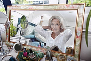 Mirror reflection of senior woman putting on necklace at home photo