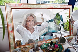 Mirror reflection of senior woman putting on necklace at home photo