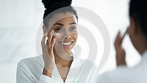 Mirror reflection smiling African American woman applying moisturizing cream