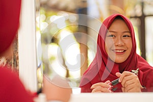 Mirror reflection of young happy and beautiful Muslim woman in traditional hijab head scarf applying make up and cosmetics