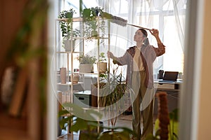 Mirror Reflection of Young Woman Dusting Tall Shelves