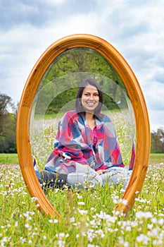 Mirror in spring meadow with sitting pretty woman