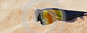 mirror sunglasses on sand on beach reflecting sea waves, suitable for header or banner