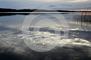 Mirror water surface reflecting sunlit clouds in evening