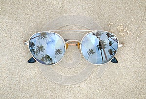 Mirrored sunglasses close up on the beach sand with palm trees reflection