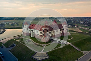 Mirsky Castle and its reflection in the lake in summer. Sunset in cloudy weather with rain clouds. Aerial view from a drone