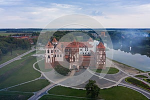 Mirsky Castle and its reflection in the lake in summer. Sunset in cloudy weather with rain clouds. Aerial view from a drone