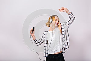 Mirthful gorgeous girl with closed eyes enjoying music, dancing and holding smartphone in hand. Party atmosphere