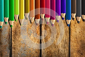 Misaligned coloured pencils on wooden desk background