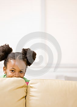 Mischievous African girl hiding behind sofa