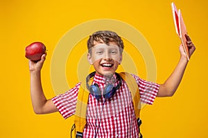 Mischievous boy with backpack and headphones holds books and Apple in his hands