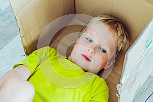 Mischievous boy play hiding in box because does not want to go to school or kindergarten on the first day of school in